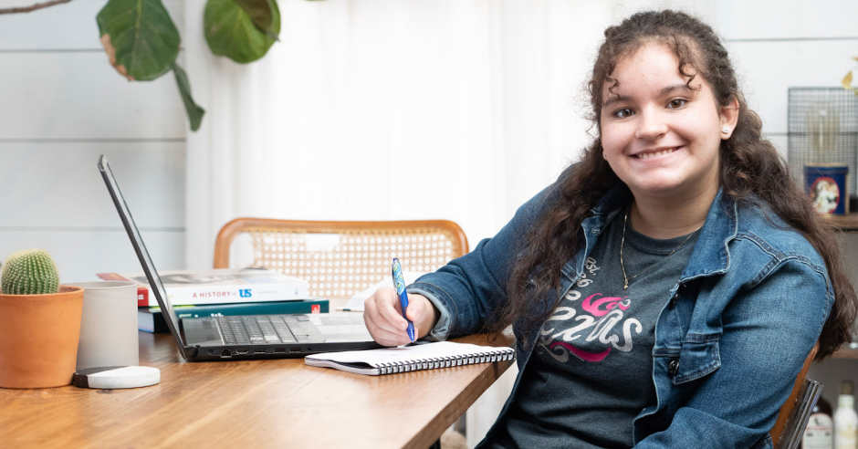 Student smiling to the camara, sitting on her table with her laptop image
